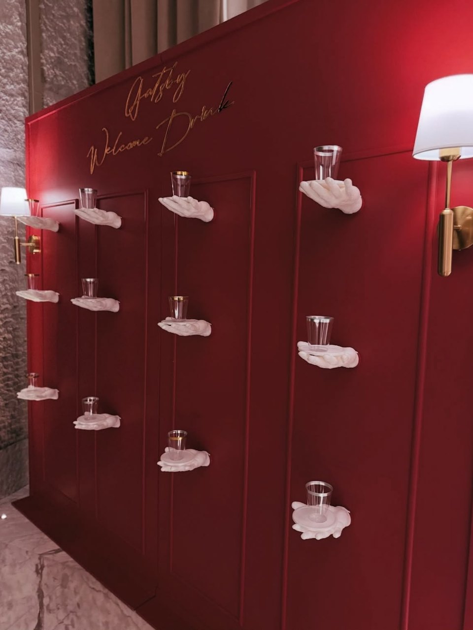 Gatsby-themed welcome drink wall with sculpted hand shelves holding glasses by DT Events