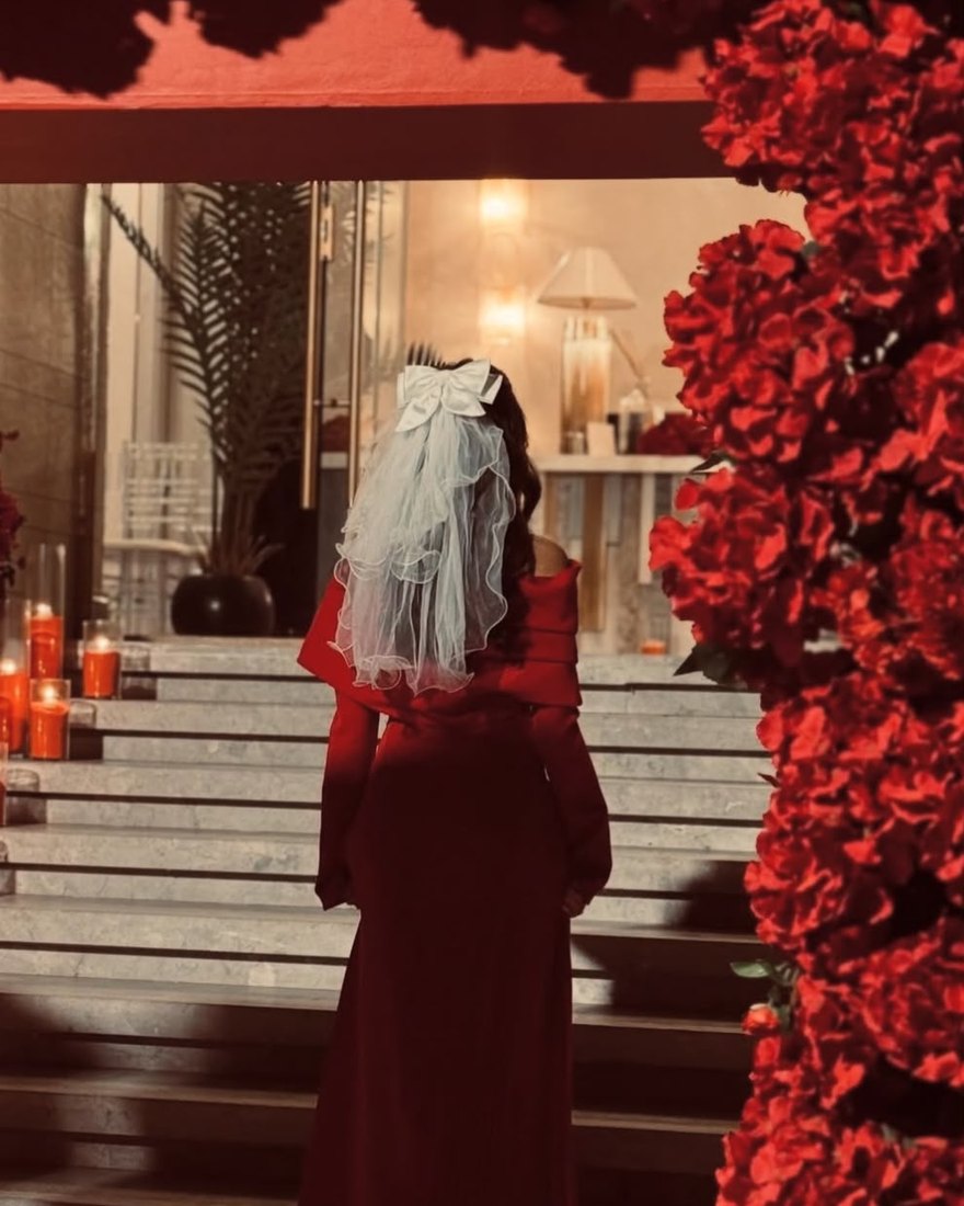 Bride in red with a bow veil on a candle-lit staircase framed by red roses, by DT Events