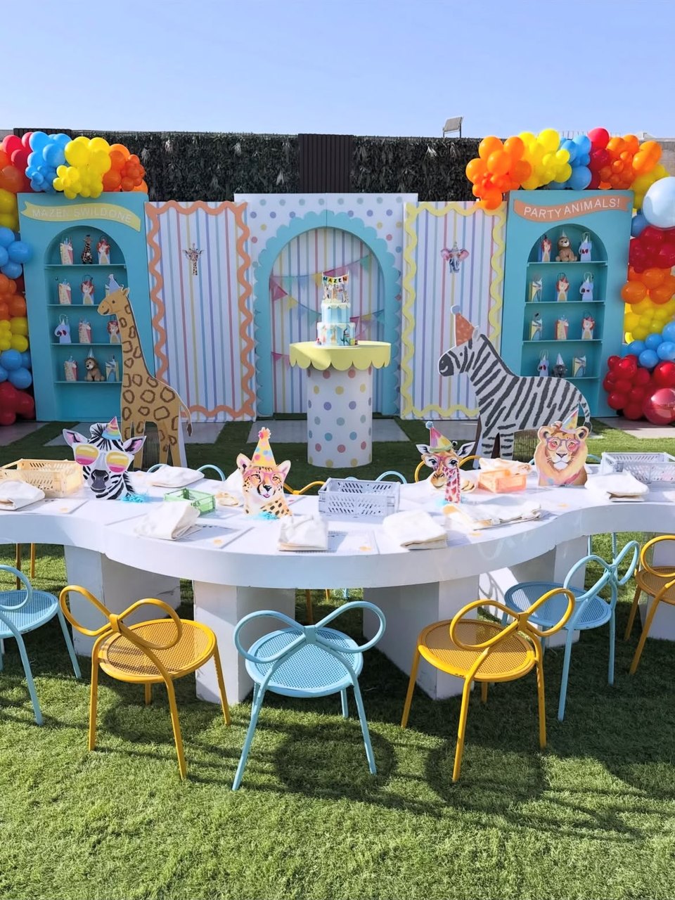 Animal-themed first birthday party set-up with balloon arches and a pastel cake table by DT Events